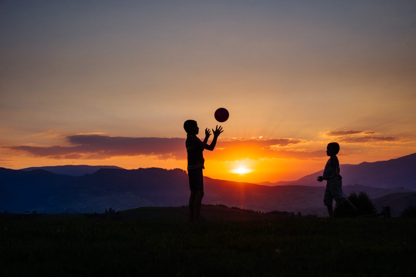 Zwei Kinder spielen mit Ball im Sonnenuntergang